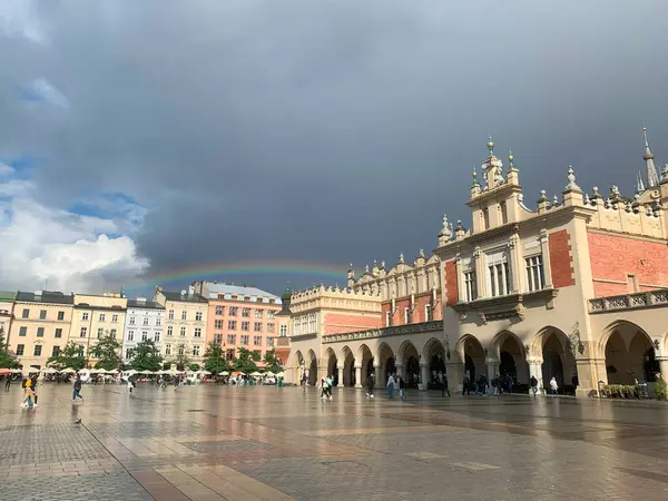 Bulutlu bir gökyüzü ile tarihi bir Avrupa meydanının üzerinde bir gökkuşağı belirir. Krakow 'da Gökkuşağı