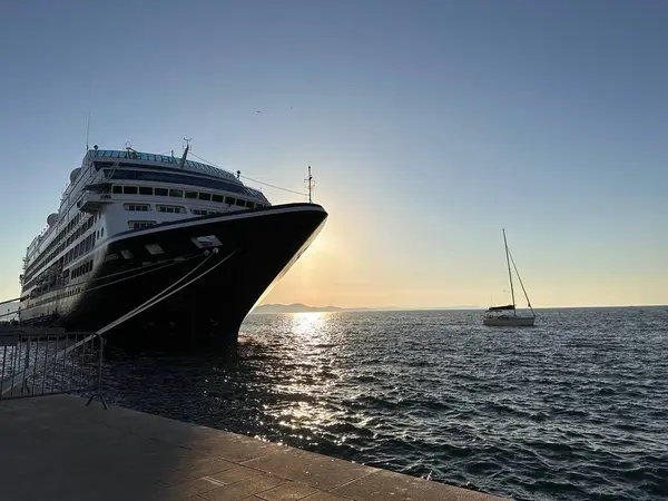 Gün batımında büyük bir yolcu gemisi sakin sularda bir yelkenliyle yanaştı.