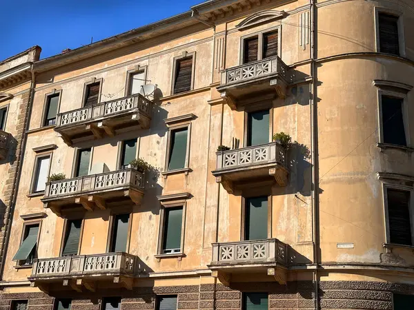 Süslü balkonları ve kapalı panjurları olan, sıcak güneş ışığıyla yıkanmış klasik mimari detaylar ve yıpranmış bir cephe içeren klasik bir Avrupa apartmanı..