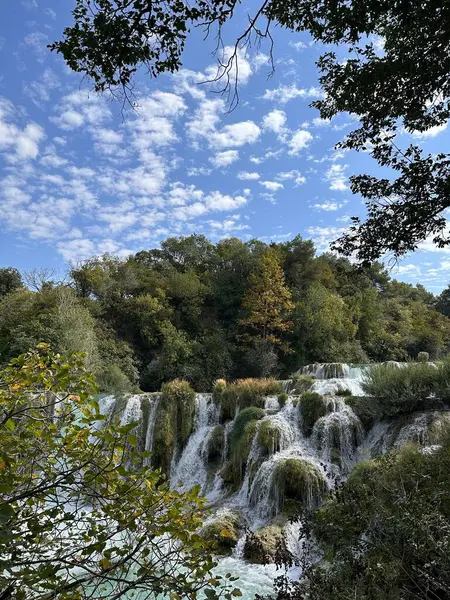 Manzaralı şelale, bulutlu bir gökyüzünün altında yemyeşil kayaların üzerinde çağlıyor..