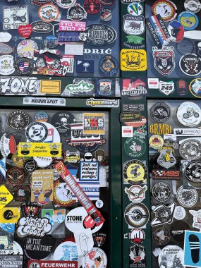 Farklı marka ve kuruluşlardan logoların, sloganların ve grafiklerin yer aldığı cam yüzeydeki çeşitli çıkartmaların renkli bir kolajı, canlı ve seçici bir görsel yaratıyor..