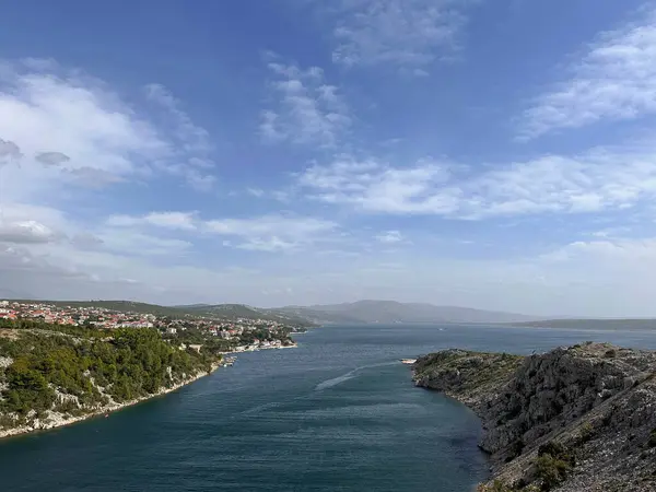 Kayalık uçurumlarla ve mavi gökyüzünün altındaki uzak bir kasabayla kıyı koyunun manzarası.