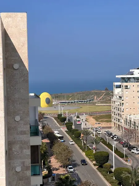 Modern binalar, bir yol ve berrak mavi gökyüzünün altında uzak bir deniz manzarası olan bir sahil şehri..