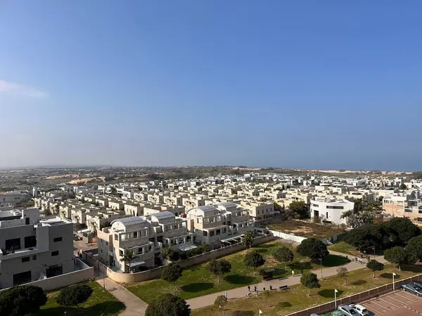 Üniformalı beyaz evler, yeşil alanlar ve açık mavi gökyüzü olan banliyö yerleşim alanının havadan görüntüsü..