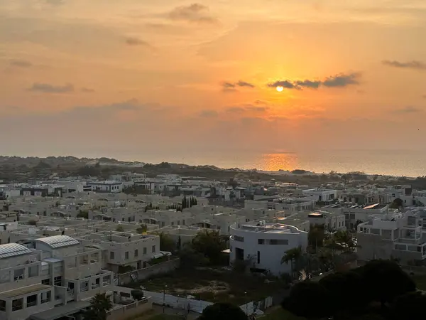 Günbatımında modern beyaz binalar ve deniz manzaralı bir sahil kasabası..