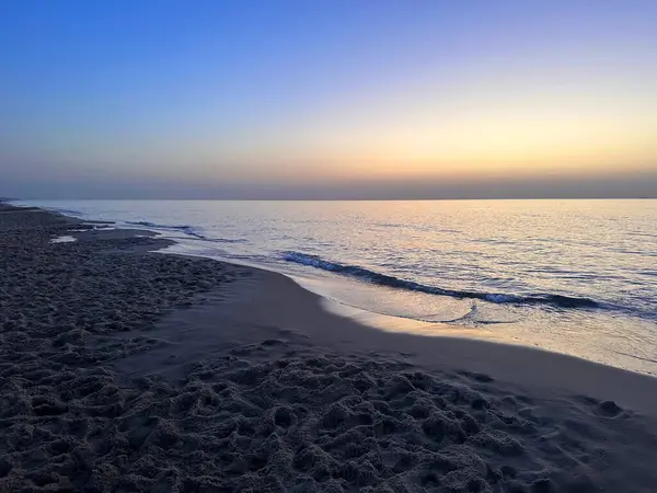 Gün batımında sakin bir sahil, yumuşak dalgalar ve berrak bir gökyüzü..