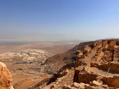 Kayalık bir çöl arazisindeki eski kalıntılar berrak mavi gökyüzünün altında uzak bir su kütlesi..