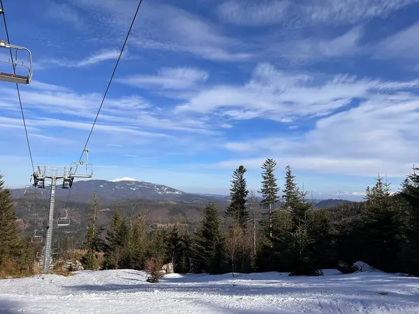 Bir kayak kaldıracı, karla kaplı zemin ve ince bulutlu mavi gökyüzünün altındaki uzak dağlar içeren manzaralı bir kış manzarası..