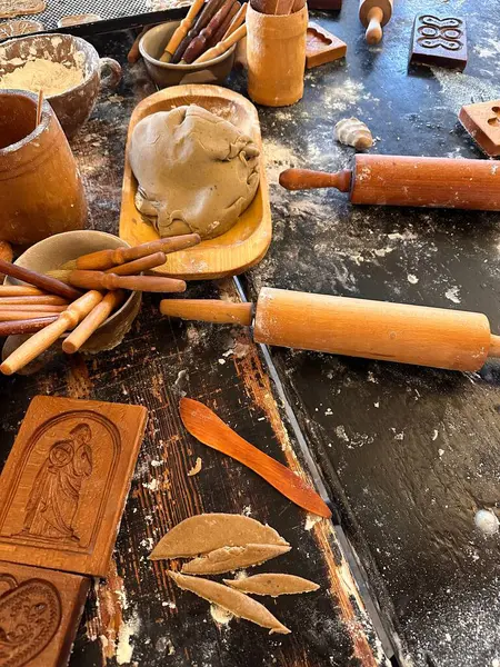 Çömlek aletleri ve malzemelerle dolu kırsal bir çalışma alanı. Yuvarlanan raptiyeler, kil ve ahşap çatal bıçaklar dokulu bir masa yüzeyine saçılmış vaziyette çömlek yapma sanatını sergiliyorlar..