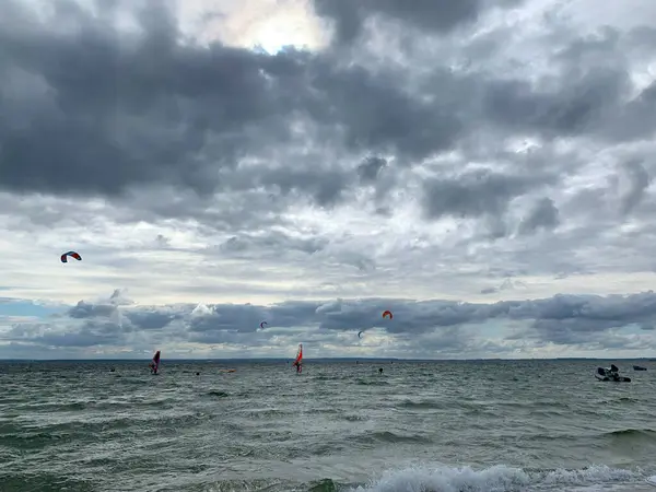 Uzakta birkaç uçurtma sörfçüsüyle bir su kütlesi üzerinde bulutlu bir gökyüzünün manzarası. Okyanus dalgaları yavaşça dönüyor ve atmosfer dinamik ve maceraperest..