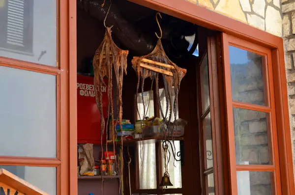 Kapıda asılı duran kurutulmuş ahtapot geleneksel deniz mahsullerini koruyor. Sahne, taştan duvarlar ve ahşap aksanlı kırsal bir cazibeyi yakalıyor..