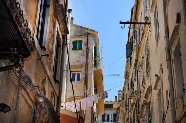 Tarihi bir kasabada dar bir ara sokak, yıpranmış yüzleri olan eski binalar. Elbiseler açık mavi gökyüzünün altında, binalar arasında bir çizgide asılı duruyor..