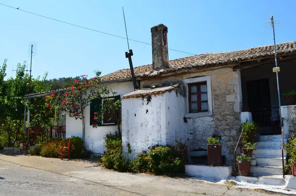 Taş duvarı, bacası ve fayanslı çatısı olan güzel bir köy evi. Ön bahçede çiçekler ve yeşillikler sergileniyor, resim gibi bir manzara yaratıyor. Huzurlu ve davetkar bir ortam, köyün tipik bir örneği..