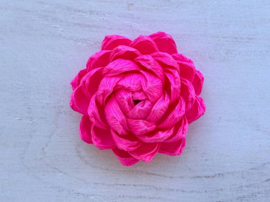 Krep kağıdından yapılmış parlak pembe el yapımı çiçek. Dekorasyon ve el işi projeleri için kullanılan hafif ahşap arka plana yerleştirilmiş..