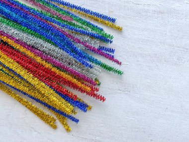 Altın, gümüş, kırmızı, mavi, yeşil ve pembe tonlarda renkli metal boru temizleyiciler, ışık arka planına çapraz yerleştirilmiş, Noel zanaatları, şenlik dekorasyonları ve DIY projeleri için kullanılır..