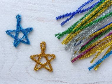 Mavi ve altın el yapımı yıldız süslemeleri. Metalik boru temizleyicilerden yapılmış. Arka planda renkli teller var..