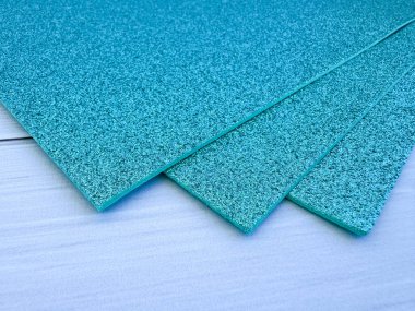 Several turquoise glitter foam sheets stacked together on white wooden surface. Perfect for craft projects, DIY, decor and creative art ideas.