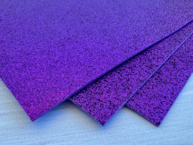 Several purple glitter foam sheets stacked together on white wooden surface. Perfect for craft projects, DIY, decor and creative art ideas.