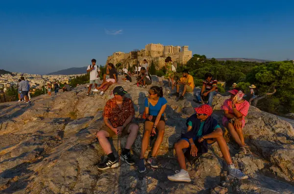 ATİNA, GREECE -- 19 Ağustos 2020 -- Yunanistan 'ın başkenti Atina' daki Partenon 'un altındaki Aeropagus Tepesi' nde oturan turistler