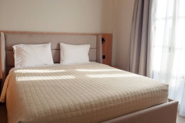 Otelde bir yatak, iki yastık ve beyaz bir battaniye. Penceresi ve perdesi olan bir odada.