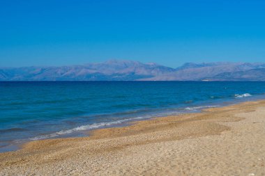 Açık mavi bir okyanusu ve kayalık bir kıyısı olan bir sahil. Kumsal boş ve gökyüzü temiz.