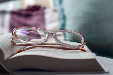 A pair of glasses is on top of a book. The book is open to a page with a purple background
