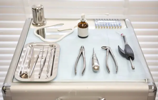 Steril bir tepsiye yerleştirilmiş paslanmaz çelik diş aletlerinin yakın plan görüntüsü. Bu araçlar arasında, modern bir diş kliniğinde genellikle sözlü muayeneler, temizleme ve çıkarmalar için kullanılan sondalar, forseps ve asansörler bulunmaktadır..