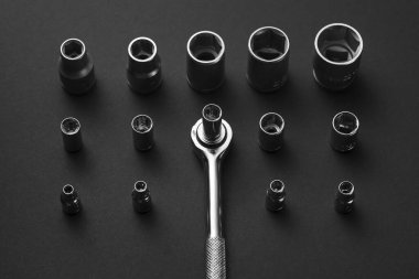 Krom soket anahtarlar ve adaptörler koyu gri bir yüzeye yerleştirilmiştir. Anahtarların boyutu ve şekli farklı, ön planda tek bir anahtar kolu görünüyor..