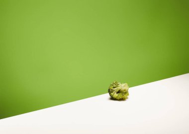 Canlı yeşil arka planlı beyaz masanın üzerinde küçük bir parça taze brokoli