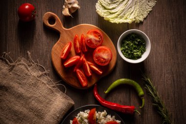 Kırsal bir ahşap kesim tahtası canlı taze sebze çeşitleri sergiler. Tahtada olgun domates dilimleri, tek bir vişneli domates ve doğranmış beyaz lahana var..