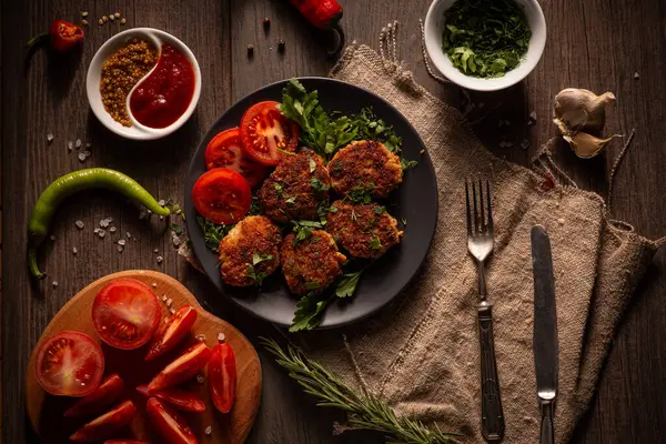 Karanlık, karamsar bir fotoğraf, içinde taze domatesler, otlar ve bir tutam sosla süslenmiş küçük yuvarlak köfteler sergiliyor. Tabak kırsal bir ahşap masada duruyor.