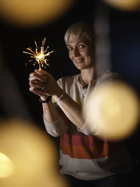 Gülümseyen bir kadın elinde bir maytap tutuyor, mumların ışığıyla aydınlatılıyor. Çizgili bir kazak ve kolye giyiyor. Yeni yıl ve Noel kompozisyonu