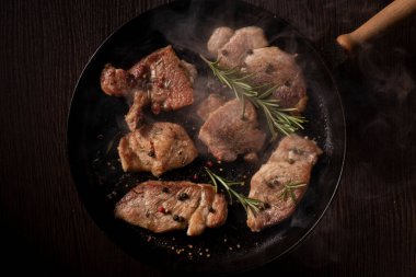 Siyah dökme demir tavada pişmiş bifteğin cızırdayan birkaç parçasının yakın plan çekimi. Biftek kahverengileşmiş ve hafifçe yanmış, buhar çıkarıyor..