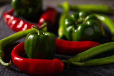 Koyu renkli bir natürmort fotoğrafında desenli gri bir yüzeye yerleştirilmiş taze biber koleksiyonu sergileniyor. Birkaç yeşil dolma biber. Biberler şekil ve boyut olarak değişir.