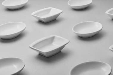 Gri bir yüzeye yerleştirilmiş küçük, beyaz seramik çanak koleksiyonu. Tabaklar oval, kare ve dikdörtgen formlar da dahil olmak üzere şekil olarak değişir. Aynı boyuttalar.