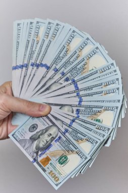 Tarafsız bir arkaplanda Amerikan doları banknotlarını tutan bir elin yakın çekimi. Ödeme, kazanç, mali başarı, maaş, yatırım veya bankacılık ve iş kavramı.