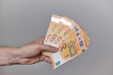 Temiz ve nötr bir arkaplanda avroya ait çeşitli banknotları tutan bir insan elinin yakın çekimi. Finans, maaş, yatırım, tasarruf veya ödeme kavramı.