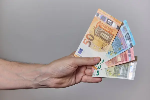 Temiz ve nötr bir arkaplanda avroya ait çeşitli banknotları tutan bir insan elinin yakın çekimi. Finans, maaş, yatırım, tasarruf veya ödeme kavramı.