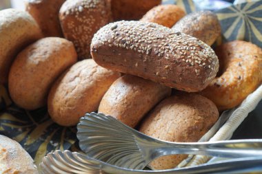 Açık büfedeki kahverengi ve beyaz çörekleri metal maşayla yakın plan çek..