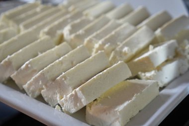 Paslanmaz çelik bir büfe tepsisinde düzgün düzenlenmiş yumuşak beyaz peynir küplerinin yakın çekimi..