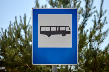 Üzerinde otobüs işareti olan mavi kare yol tabelası resmi bir otobüs durağının yerini gösteriyor. Sürücü ve yolculara rehberlik ederken, toplu taşıma araçlarının belirlenen noktalarda güvenli bir şekilde durmasını sağlamak.