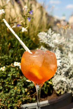 Aperol spritz kokteyli yeşil arka planlı bir açık hava yüzeyinde duruyor.