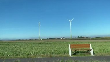 Yeşil çimenler ve mavi gökyüzü ile kırsal alanda dönen uzun rüzgar türbinleri