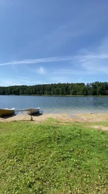 Yeşil çimenli göl kıyısında durgun suyun yanında birkaç tekne var.