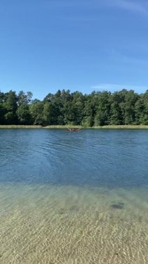 İnsanlar uzakta ormanlık alanda sakin göl suyunda kano yapıyor.