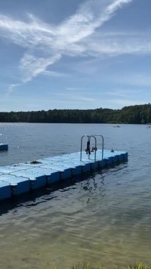 Ufukta ağaçlar ve sakin göl suyunda yüzen mavi plastik iskele.