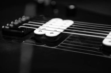 Makro, elektro gitar köprüsünün ve monokromda yakalanan pikapların yakın plan fotoğrafı. Güçlü dokular ve keskin detay ustalığı ve rock enstrümanı stilini vurguluyor.