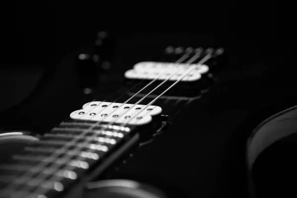 Elektro gitarın siyah ve beyaz yakın plan fotoğrafı dramatik ışıklandırma, vurgulu doku, işçilik ve müzik aleti detaylarını gösteren telleri ve pikapları gösteriyor..
