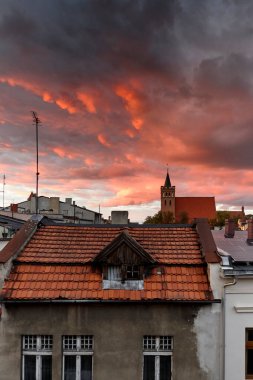 Dramatik kırmızı ve turuncu günbatımı bulutlarının altında eski bir gotik kilise kulesi olan Avrupa çatıları. Kasvetli gökyüzü çarpıcı bir akşam manzarası yaratır..