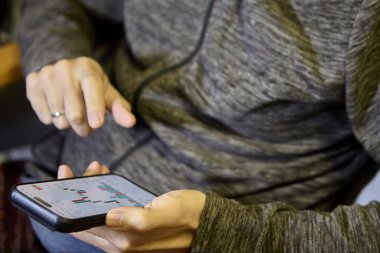 Gri kapüşonlu yetişkin akıllı telefonu iki eliyle içeri kaydırırken ekranın içeriğini görüyor